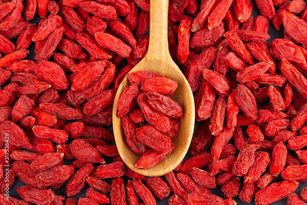 Spoon with Goji berries over red goji background. Healthy food concept.